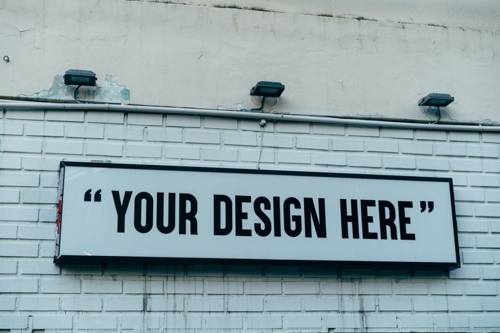 Your Design Here Sign Black and White on White Brick Wall 1200x800px